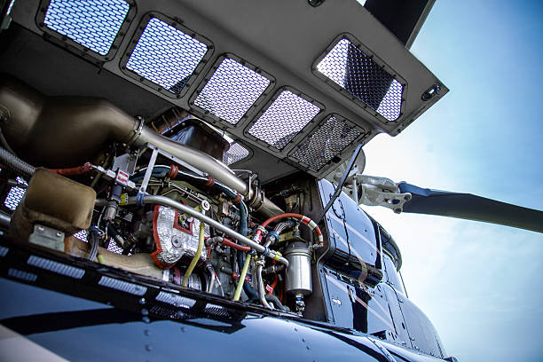 Close up of motor of black with gray stripes bell 407 helicopter standing on green grass field on blue sky background.